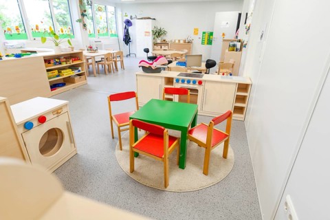 Children's room with colourful chairs and a small play kitchen on carpet, transitional daycare