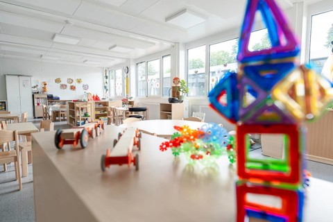 Colourful kindergarten room with toys and large windows, flooded with light, transitional