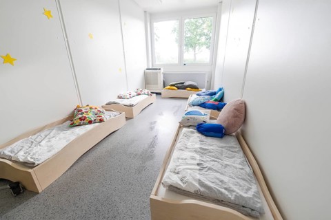 A bright bedroom with several small beds and colourful cushions, transitional daycare centre in