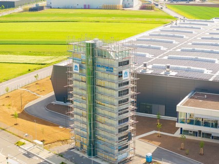 Industrial building with scaffolding and solar panels, surrounded by green fields, ING Park