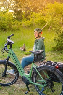 Person with helmet sitting in the sunset next to a bicycle in a meadow, surrounded by nature,