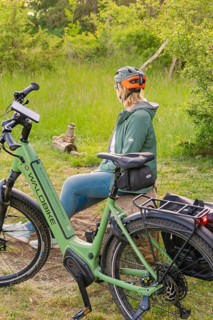 A person wearing a bicycle helmet sits on a tree stump next to a bicycle in the forest, e-bike