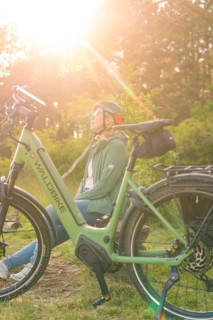 Person with helmet sitting next to a bicycle, enjoying nature in the warm sunlight, e-bike