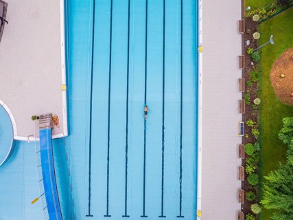 A swimmer swimming laps in a large swimming pool surrounded by green areas, Calw outdoor pool,