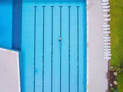 Drone shot of an empty swimming pool with a swimmer in a turquoise-coloured pool on a summer's day,