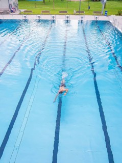 A swimmer swimming steady laps in a calm blue pool, Calw outdoor pool, Black Forest, Germany