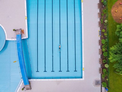 A swimmer in the large, empty pool, surrounded by paved paths and greenery, Calw outdoor pool,