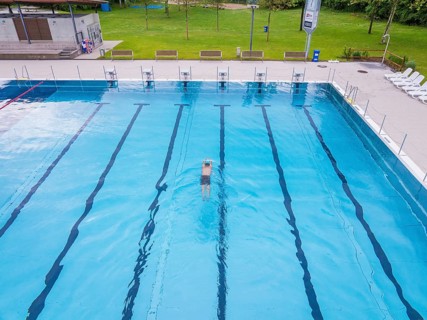 A swimmer swims in the large, clear pool on a sunny day, Calw outdoor pool, Black Forest, Germany