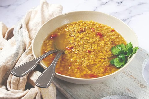A hearty lentil soup is beautifully presented in a beige bowl, garnished with fresh herbs, placed