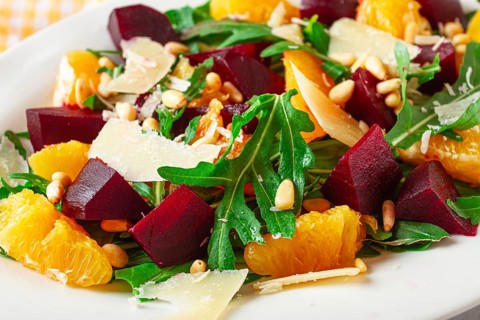 A salad made with chunks of beet, orange slices, and arugula. It is topped with cheese shavings and