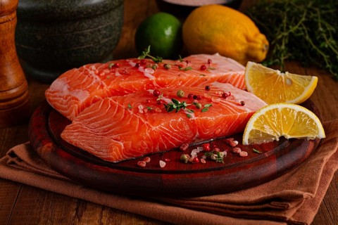 Two salmon fillets rest on a wooden platter. The fillets are garnished with herbs and spices. Lemon
