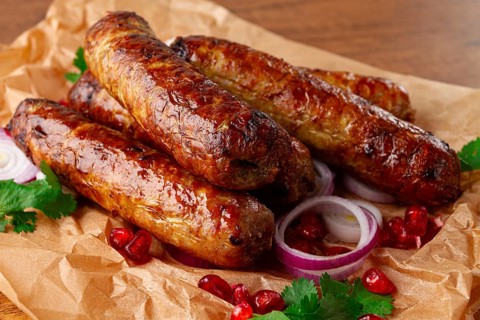 Fried kupaty on parchment, with red onion and pomegranate, kupaty, Georgian cuisine