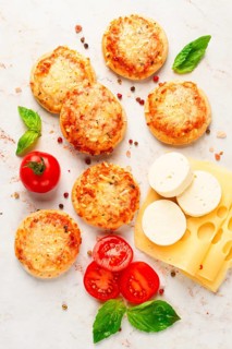 Freshly baked mini pizza on a marble table, with fresh vegetables and cheese, top view