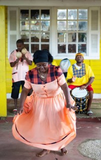 Guatemalan woman in traditional dress singing and dancing, men playing music in the back, Garifuna