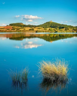 Wachsenburg Castle is reflected in the still water of a lake under a blue sky with cumulus clouds,