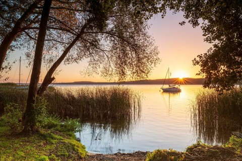 Sunrise at a swimming area on Schwielowsee near Potsdam, sailboat anchored in water, reeds and