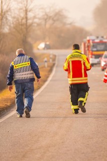 Rescue workers walk on a country road while emergency vehicles are visible in the background, fire