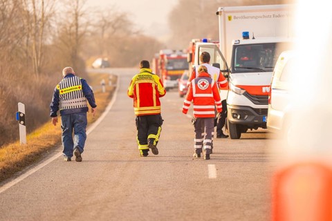 Emergency personnel from various services walk on a country road, accompanied by emergency