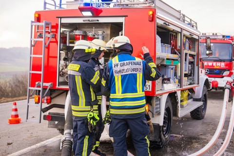 Firemen in emergency clothing stand at an emergency vehicle and check hoses, fire brigade exercise