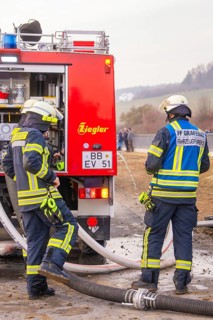 Firemen deployed next to a red fire truck. They wear helmets and special uniforms, fire department