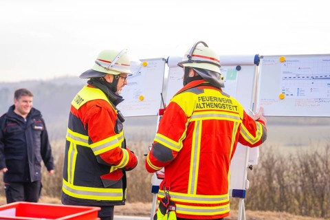 Firefighters in operational clothing during mission briefing in front of a rural backdrop, fire