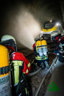 Firefighters with respirators extinguish a fire in a tunnel using water hoses, fire brigade