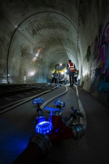 Workers in the dark railroad tunnel. Lighting and technical equipment are visible, fire department