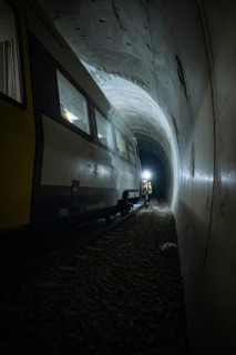 Light beam illuminates workers next to a train in a dark tunnel, fire department exercise on the