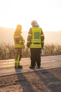 Two firefighters in protective clothing stand on a street at sunset, fire brigade exercise on the
