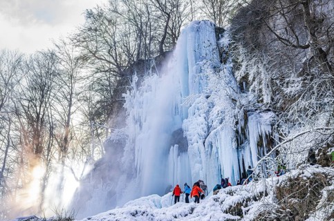 Spectators climb on the Urach waterfall full of bizarre ice formations, frozen at low winter