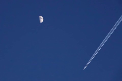 Airplane with contrails and moon in the evening sky, Germany