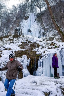 Hikers climb on the Urach waterfall full of bizarre ice formations, frozen at low winter