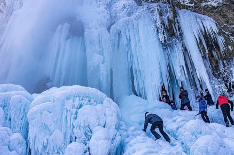 Spectators climb on the Urach waterfall full of bizarre ice formations, frozen at low winter