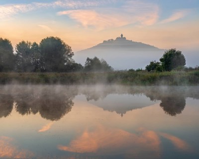 Wachsenburg Castle is reflected in the still water of a lake at sunrise, fog rises, castle of the