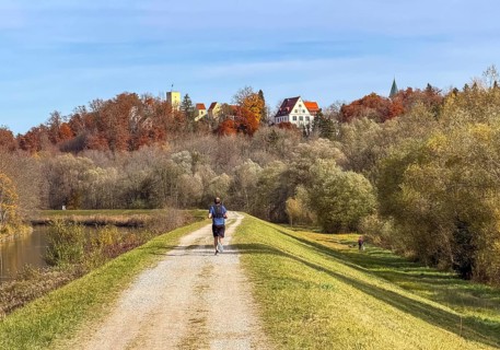 Jogger on a path along the Isar with a view of Grünwald with Bürg Grünwald, Grünwald, Bavaria,