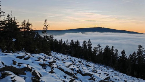 Landscape with snow-covered ground, trees and a mountain in the evening light, thick fog over the