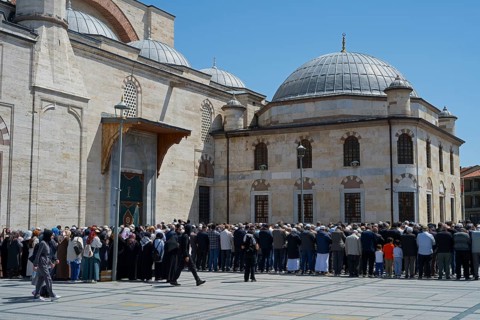 People gather in front of a large stone building with domes on a sunny day, prayer in front of the