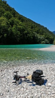 A bicycle is lying on a pebble beach by a river with clear water and wooded banks, Soca Valley,