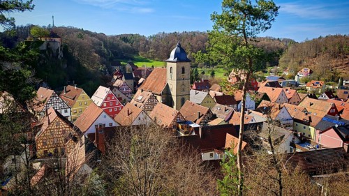 Picturesque village with colorful half-timbered houses and church tower, surrounded by hills, view