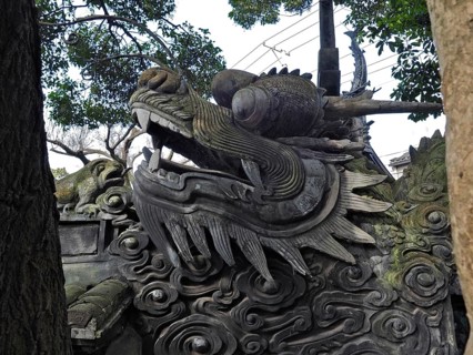 A detailed stone dragon statue surrounded by trees, with a powerful and majestic expression, Yuyuan