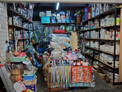 Small shop with a variety of everyday items on densely packed shelves and tables, Wet Market,