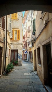 Narrow alley with historic buildings and colorful shutters in a sunny old town, Piran, Slovenia