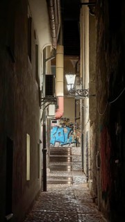 Narrow, illuminated alley at night with stairs lined with graffiti and old architecture, Ljubljana,