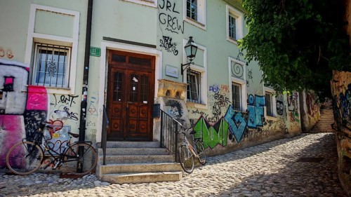 A paved street with ornate graffiti on walls and two bikes in front of a historic building,