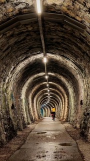 An illuminated tunnel with stone walls and a cyclist in the distance, Slovenia