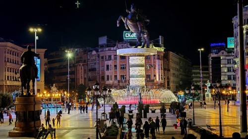 Illuminated square at night with equestrian statue and bubbling fountain in an urban setting,
