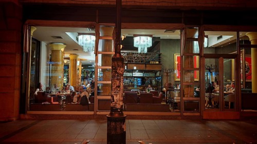 Interior view of a café with glass façade and visible guests at night, Skopje, North Macedonia