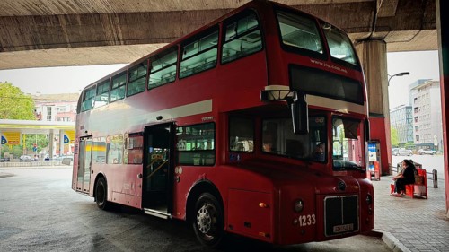 Classic red double-decker bus at a bus stop in an urban environment under a bridge, Skopje, North