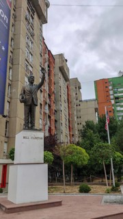 Bill Clinton statue in front of an apartment block with surrounding trees and flagpoles, Pristina,