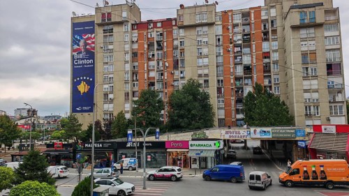 Skyscrapers with a big Bill Clinton poster, parked cars and lively streets in an urban environment,